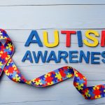 World Autism awareness and pride day or month with Puzzle pattern ribbon on blue wooden background.