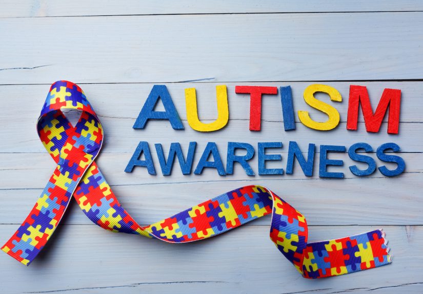 World Autism awareness and pride day or month with Puzzle pattern ribbon on blue wooden background.